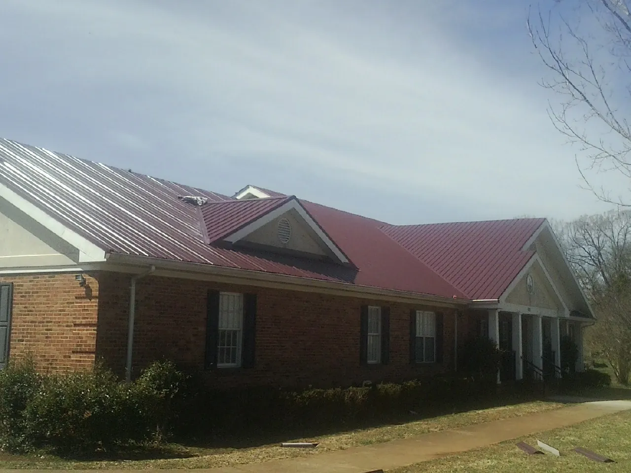 Red metal roof with gabled entries on a long brick building, from a Hail Damage Roof Repair job in New Ellenton