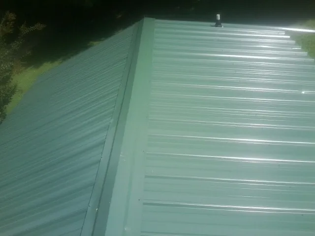 New green metal panels meeting at the ridge of a roof — Flat Roof Repair work by our crew in New Ellenton