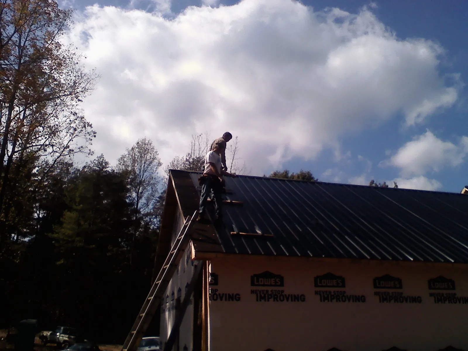 Roofer fastening dark metal panels high against a cloudy sky, from a Roof Inspection job in New Ellenton
