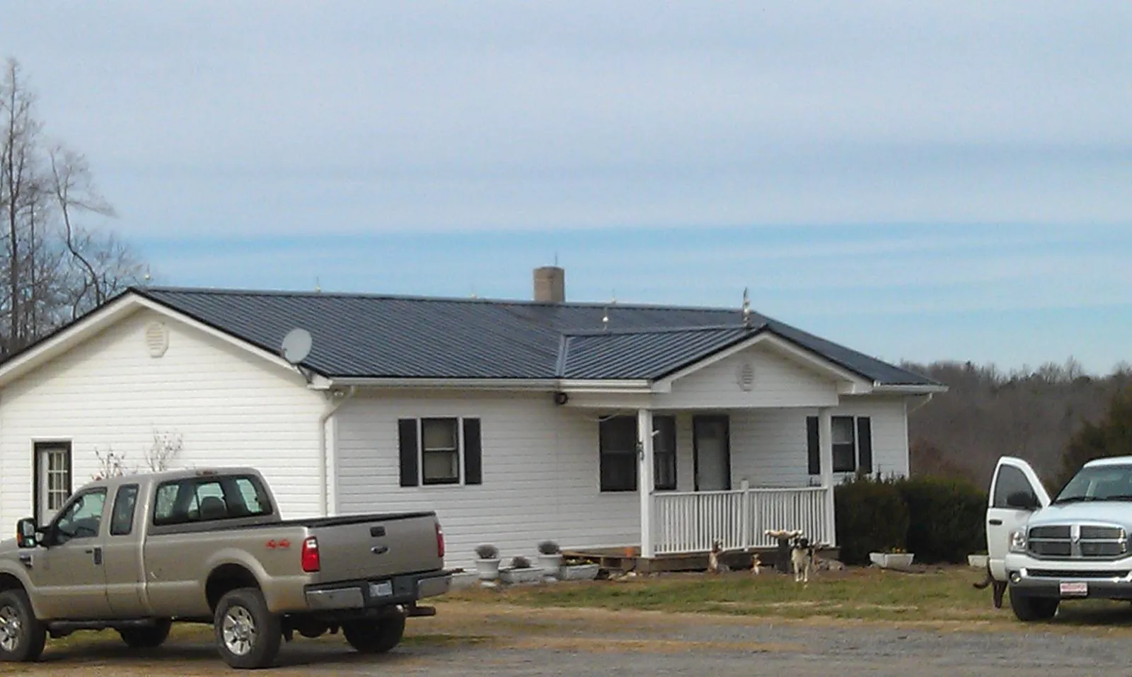 Finished dark metal roof on a white ranch home with work trucks parked in New Ellenton