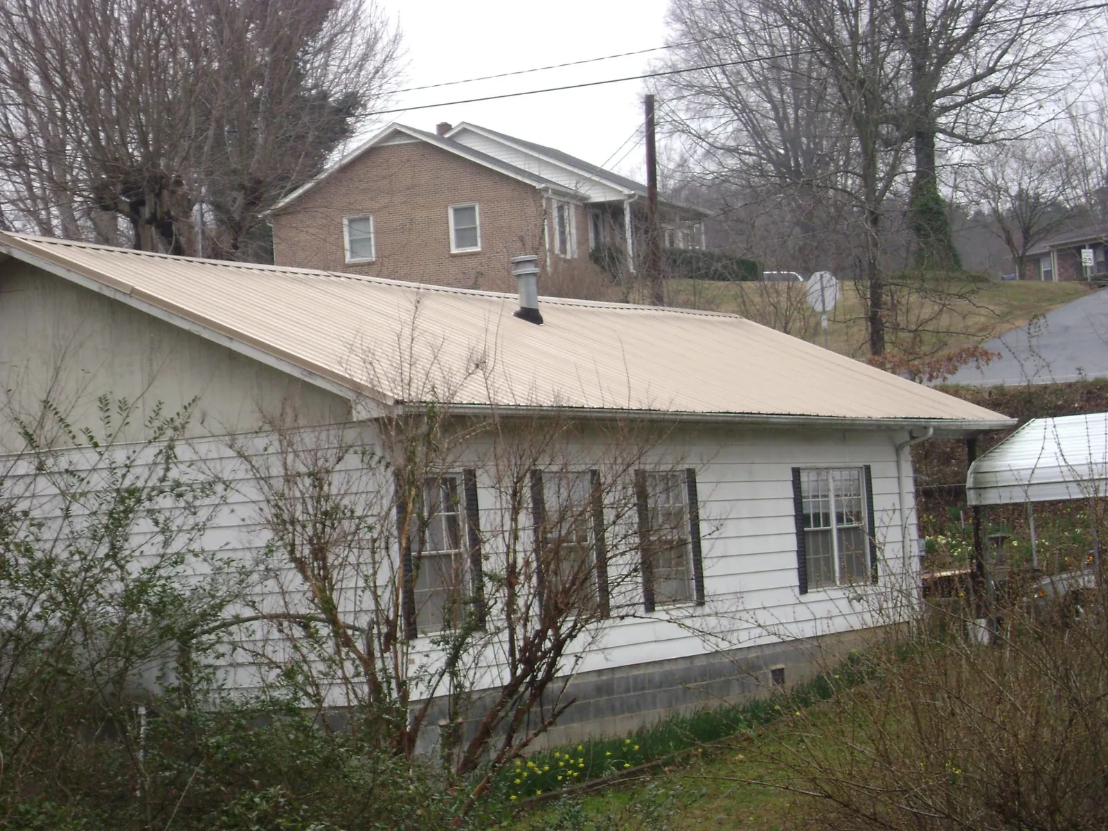 Tan metal roof on a white sided house set into a hillside — Commercial Roofing by Roofing Brothers in New Ellenton